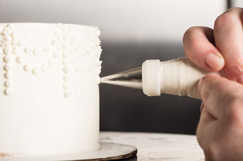 Person decorating a white wedding cake